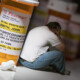 opioid addiction - man sitting beneath the shadow of a large bottle of prescription opioids