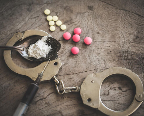 A close up of cuffs, pills, a syringe, and a powder in a spoon. A psychiatrist in New York, NY can offer treatment for opioid withdrawal in New York, NY. Learn how we can offer online opioid treatment in New York, NY and other services today.
