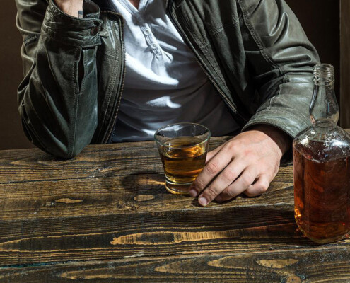 close up of man in a bar with glass and bottle of alcohol