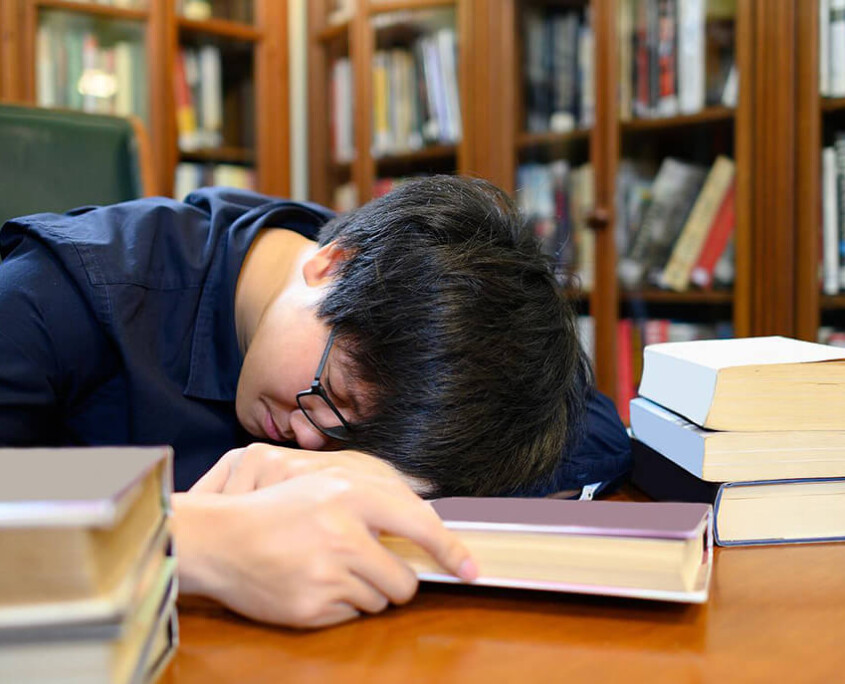 A college students sleeps with their head down while surrounded by books. Learn more about the support a drug addiction therapist in New York, NY can offer by searching for prescription drug addiction treatment in New York, NY today. A psychiatrist in New York, NY can offer support today.