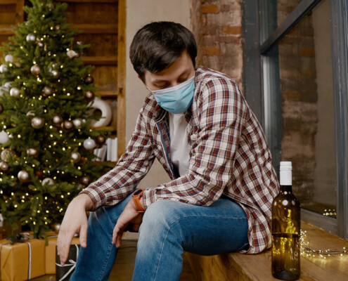 alcohol addiction - man during pandemic wearing mask looks at bottle of alcohol