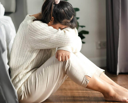A woman sits against her bed while hiding her face. Learn how an addiction therapist in New York, NY can offer support in addressing depression and substance abuse. Contact a drug addiction therapist in New York, NY for support today.