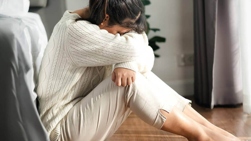 A woman sits against her bed while hiding her face. Learn how an addiction therapist in New York, NY can offer support in addressing depression and substance abuse. Contact a drug addiction therapist in New York, NY for support today.