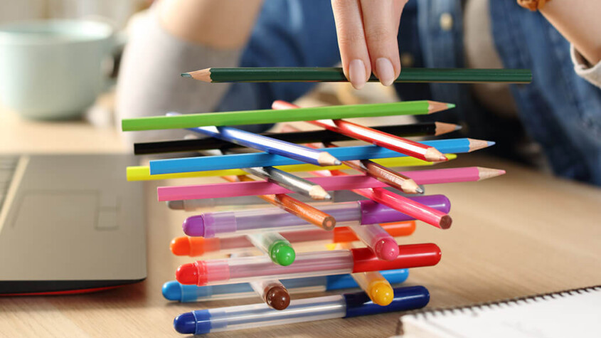Distracted woman with ADHD builds lattice of pens and pencils on her office desk