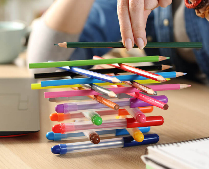 Distracted woman with ADHD builds lattice of pens and pencils on her office desk
