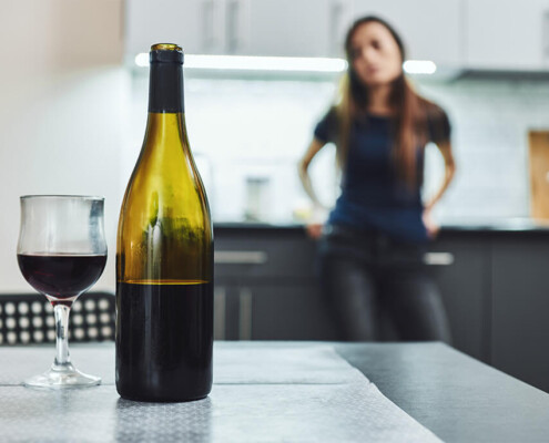 alcohol addition - woman gazes at wine bottle and glass of wine