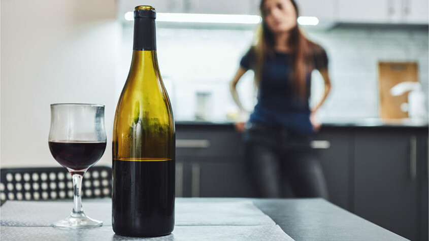 alcohol addition - woman gazes at wine bottle and glass of wine