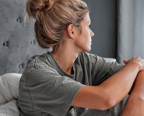 Woman struggling with PTSD and Addiction sits alone on a bed