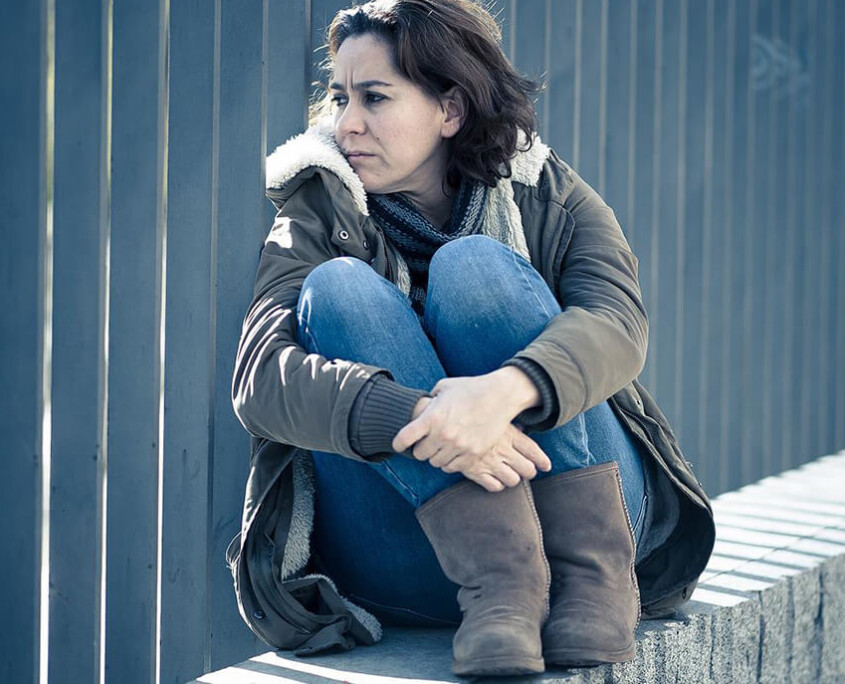 A woman sits alone next to a fence with a blank stare. This could represent the isolation felt from the stigma of addiction. Learn more about addiction treatment in New York, NY and the support an addiction therapist in New York, NY can offer today.