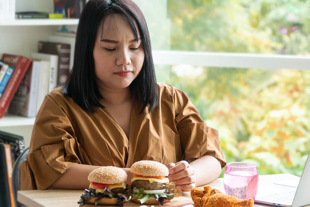 Distraught woman with a plate of unhealthy food. This could represent food addiction that behavioral addiction treatment in New York, NY can address. Learn more about from a behavioral therapist in New York, NY or addiction therapist in New York, NY. 10022