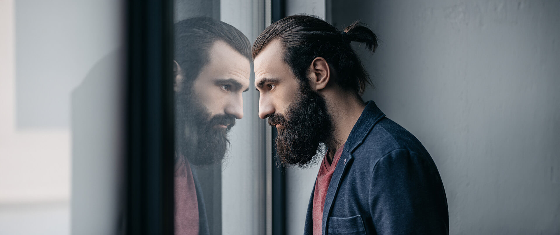 A stressed man gazes at his reflection in a window. This could represent the pain that dual diagnosis treatment in New York, NY can offer support with. Contact a dual diagnosis therapist in New York, NY to learn more about co occurring disorder treatment and other services! 10022