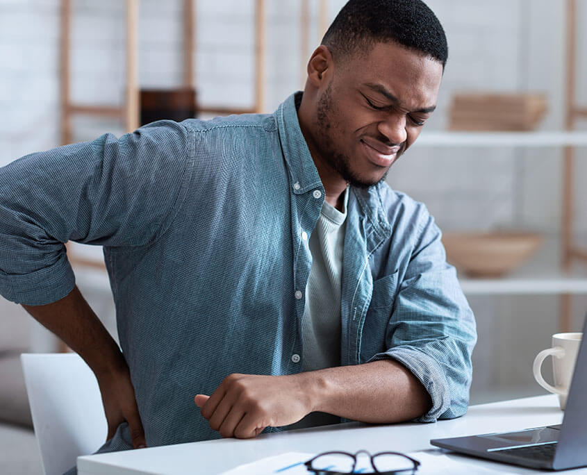 man at desk experiencing lower back pain. This represents how opioid use disorder treatment in New York, NY can help clients overcome cravings. Learn more about how opioid addiction treatment in New York, NY can help you today!