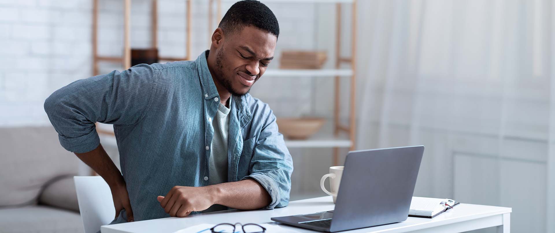 man at desk experiencing lower back pain. This represents how opioid use disorder treatment in New York, NY can help clients overcome cravings. Learn more about how opioid addiction treatment in New York, NY can help you today!