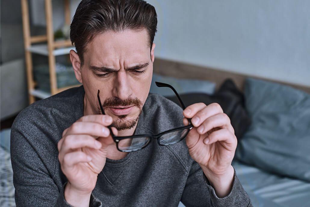 Man staring thoughtfully at his glasses. This could symbolzie the pain of addiction that psychiatry in New York, NY can help remedy. Contact a virtual psychiatrist in New York, NY to learn more about online psychiatry today! 10022