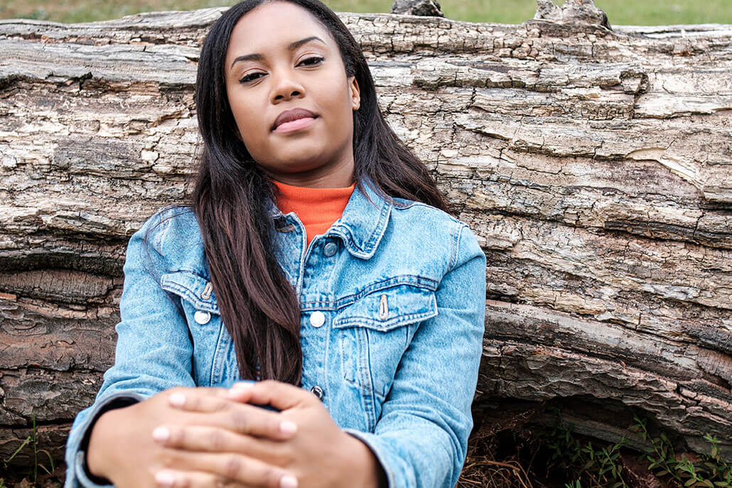 Peaceful, calm, young woman leans on a fallen tree and gazes at the camera