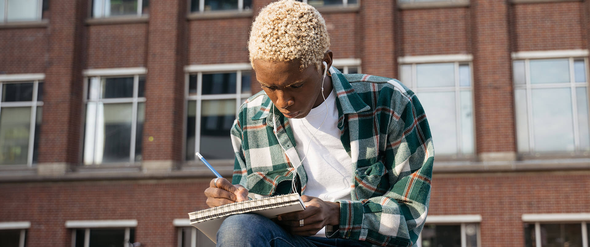 college student outside listening to lecture on mobile device and taking notes. A teenage psychiatrist in New York, NY can offer support with teenage psychiatry and other services. Contact a psychiatrist for young adults to learn about young adult psychiatry in New York, NY today!