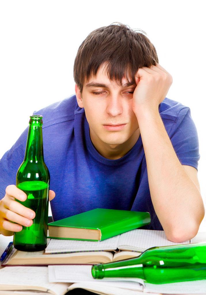 A college student holds a beer bottle above open textbooks. A psychiatrist for young adults in New York, NY can offer support via substance abuse treatment in New York, NY and more. Learn more about young adult psychiatry in New York, NY today.