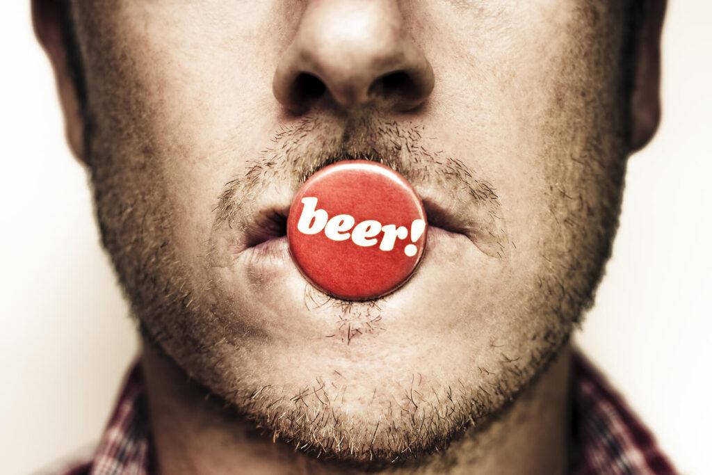 A close up of a person with a bottle cap over their lips, representing the craving for alcohol an online psychiatrist in New York, NY can address. Learn more about alcohol addiction treatment in New York, NY today by contacting an adult psychiatrist today. 
