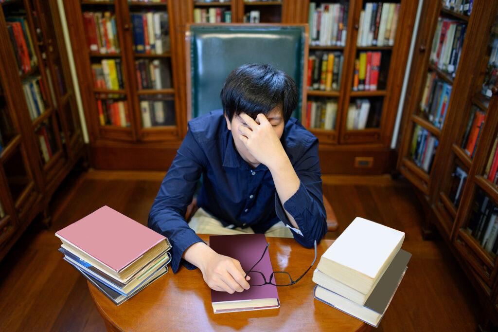 A student in a library touches their face with a tired expression. Learn how a drug addiction therapist in New York, NY can help college students via prescription drug addiction treatment in New York, NY today. 