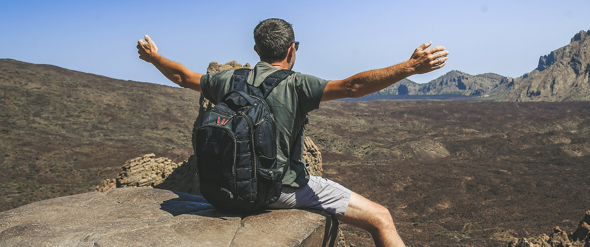 Man sitting on a rock with arms extended over an expansive landscape.